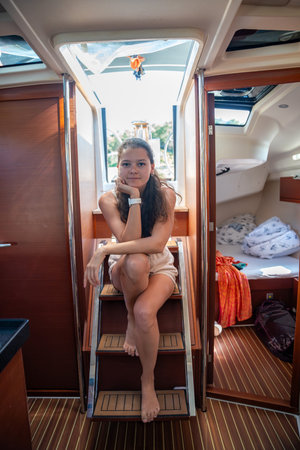 Young woman sits on the steps leading from the cockpit to the cabin of a yacht during sailing in...