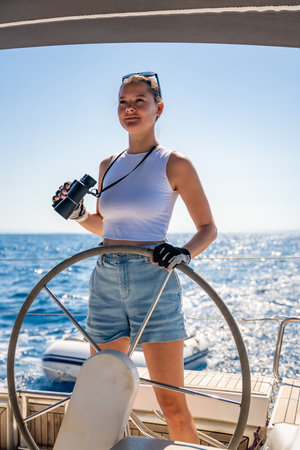 Young female captain on the yacht looking through binoculars during sailing boat control. Travel and active life. Yachting High quality photoの写真素材