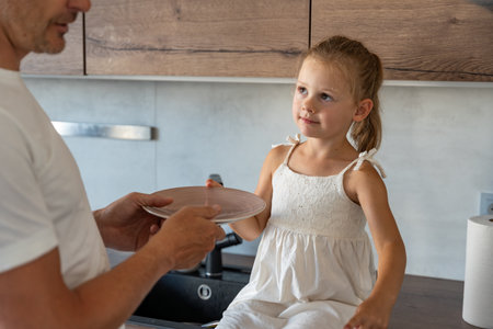 Young father and daughter cooking fish with stove together in home kitchen, giving a plate to put food on. High quality photoの写真素材