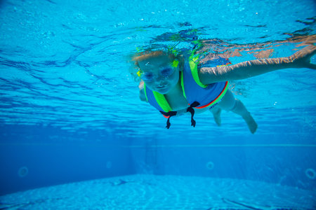 Portrait of little girl swimming underwater in goggles and vest in pool. Summer vacation. High quality photoの写真素材