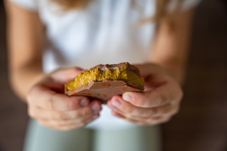 Dubai chocolate with pistachio paste and kataifi dough in hands of little girl. Confectionery handmade sweets at home in the kitchen. High quality photoの写真素材