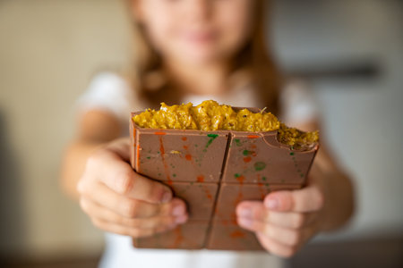 Dubai chocolate with pistachio paste and kataifi dough in hands of little girl. Confectionery handmade sweets at home in the kitchen. High quality photoの写真素材