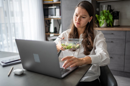 Tired woman eats food ordered at delivery service while sitting in her home office in front of laptop during lunch break. High quality photoの写真素材