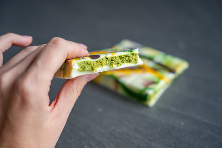 Piece of white chocolate with pistachio paste and kataifi dough in woman hand. Confectionery...