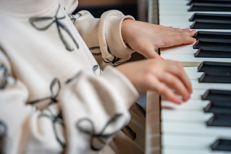 Close up view of small hands of girl on white piano synthesizer. Concept of early development: learning music enhances motor skills, hearing, and intelligence, fostering creativity from childhood.の写真素材