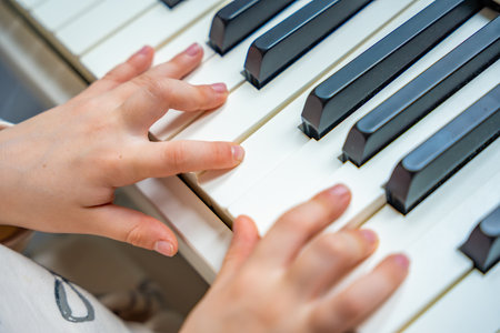 Close up view of small hands of girl on white piano synthesizer. Concept of early development: learning music enhances motor skills, hearing, and intelligence, fostering creativity from childhood.の写真素材