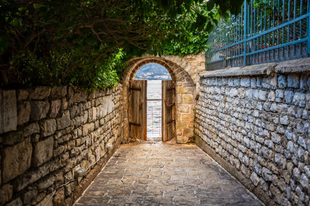 Old street in old town of Budva without people in winter time with small gate in the end to sea...