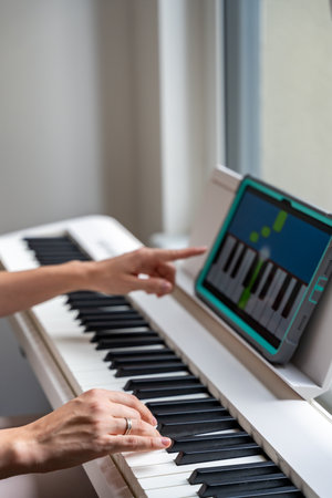 Young woman playing a keyboard while pointing at a learning app on a tablet. Technology enhances self-education in music, making learning more intuitive and engaging. High quality photoの写真素材