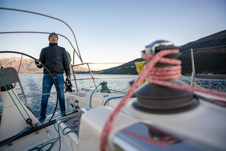 Young man captain standing at the helm and controls a sailboat during a journey by sea in winter...