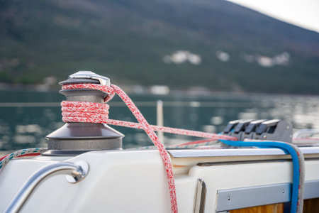 Close-up of a yacht winch with red and blue ropes secured, set against the scenic backdrop of the...