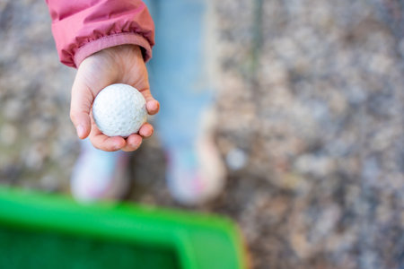 Close-Up of Child Hand Holding Mini-Golf Ball. Little girl playing mini golf outdoor. Family vacations or resort. High quality photoの写真素材