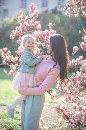 Young mother with her little daughter in a blooming magnolia garden in Prague. Symbol of maternal love and the beauty of springtime bonding in nature. High quality photoの写真素材