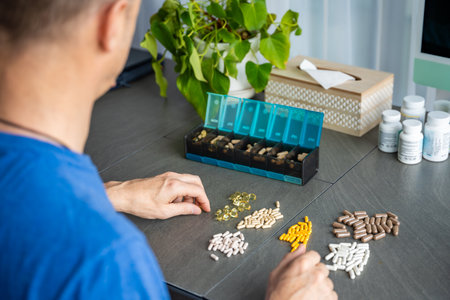 Man sorting his pills and supplements into a weekly pill organizer. Concept of medication management...