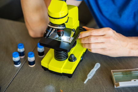 Close up view of hands of man examining various samples under a microscope at home as a hobby....