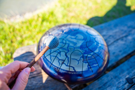 Point of view of person playing a steel tongue drum with mallets in front of mountains and river. Concept of immersive music, self-expression, and unity with natural rhythm. High quality photoの写真素材