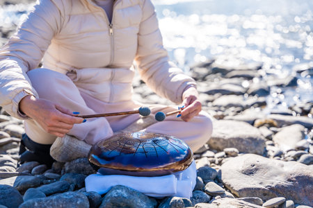 Close-up of hands playing a steel tongue drum by a mountain river in Altai. Concept of mindful music, meditative rhythm, and aesthetic harmony with wild nature. High quality photoの写真素材