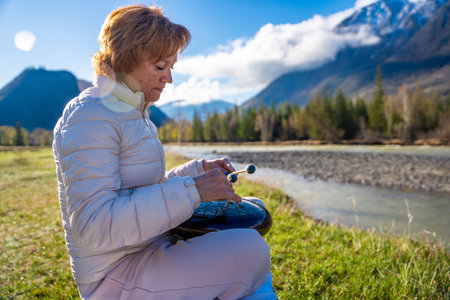 Woman playing a steel tongue drum in nature with a mountain river and Altai landscape in the...