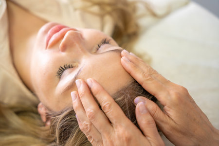 Hands of a female practitioner positioned on the face of a young woman during facial lifting session. Concept of energy work, healing touch and alternative face therapy. High quality photoの写真素材