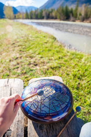 Point of view of person playing a steel tongue drum with mallets in front of mountains and river. Concept of immersive music, self-expression, and unity with natural rhythm. High quality photoの写真素材