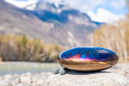 Steel tongue drum resting on a stone by the river in the Altai mountains. Concept of elemental...