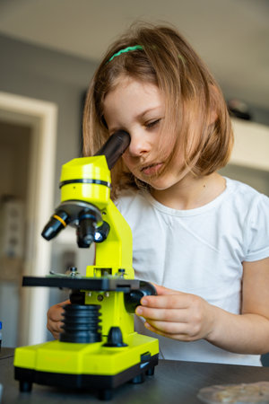 Little girl looking through a green microscope. Concept of curiosity and early scientific exploration. High quality photoの写真素材