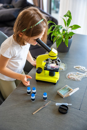 Little girl examining plant samples under a microscope at home. Concept of early science education and botanical exploration. High quality photoの写真素材