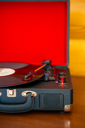 Vintage suitcase-style record player spinning vinyl record. Retro music in motion creating nostalgic atmosphere in home interior. High quality photoの写真素材