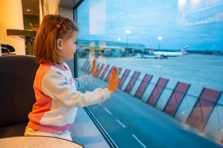 Little girl gazing out airplane window at night airport view. Concept of overnight flights, childhood travel experiences, and quiet transitions during layovers. High quality photoの写真素材