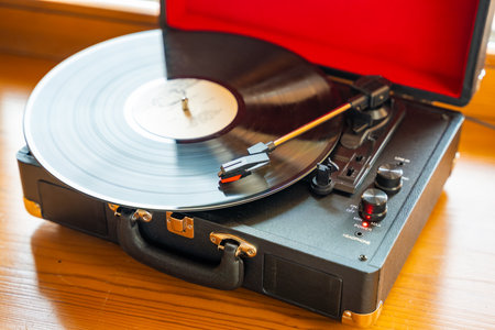 Vintage suitcase-style record player spinning vinyl record. Retro music in motion creating nostalgic atmosphere in home interior. High quality photoの写真素材