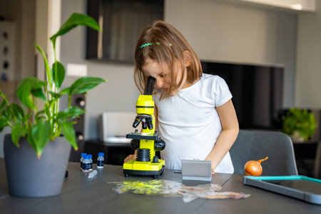 Little girl examining onion skin under a microscope. Concept of early science education and cell...