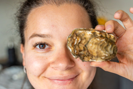 Close-up portrait of a woman holding an oyster in front of her eye. Symbol of nutrition and benefits...