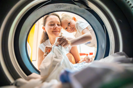 Mother and daughter doing laundry together in a self-service public laundromat, sharing household chores, building responsibility and cooperation in everyday family routine. High quality photoの写真素材