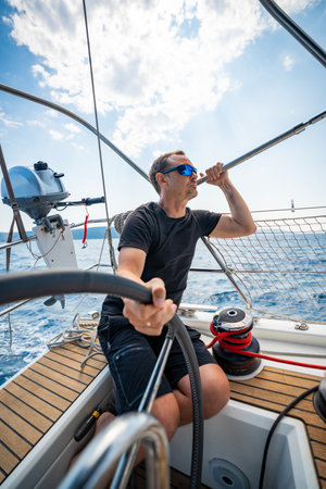Man at the helm of a sailing yacht near Croatia, steering the boat through open water. Leadership, control, sailing lifestyle and freedom at sea. High quality photoの写真素材