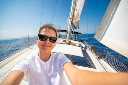 Happy young woman sitting on the bow of a sailing yacht with full sails near Croatia. Freedom, adventure, summer lifestyle and slow travel at sea. High quality photoの写真素材