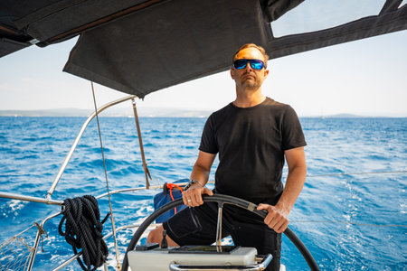 Man standing at the helm of a sailing yacht near Croatia, steering the boat through open water. Leadership, control, sailing lifestyle and freedom at sea. High quality photoの写真素材