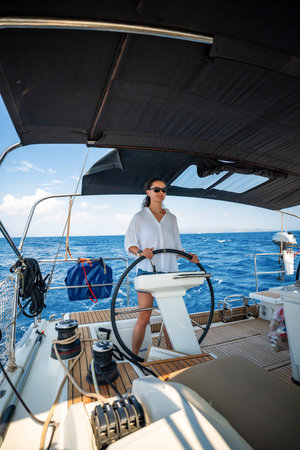 Young woman steering a sailing yacht near Croatia, confidently standing at the helm. Female leadership, empowerment and freedom in maritime lifestyle. High quality photoの写真素材