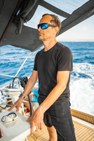 Man standing in the cockpit of a sailing yacht near Croatia, observing the sea and sails during...