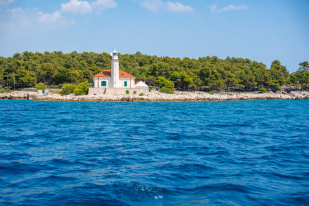 Stone lighthouse with red roof on the rocky coast of Hvar Island, Croatia, surrounded by pine trees and clear blue sea. Navigation, solitude and maritime heritage in the Adriatic. High quality photoの写真素材