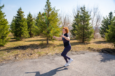 Woman jumping rope during morning workout in a green park. Cardio training, coordination, and...