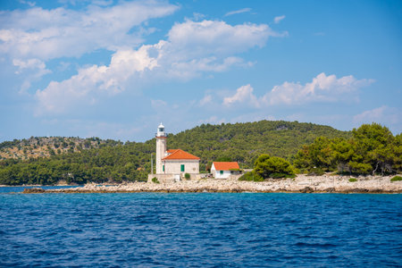 Stone lighthouse with red roof on the rocky coast of Hvar Island, Croatia, surrounded by pine trees and clear blue sea. Navigation, solitude and maritime heritage in the Adriatic. High quality photoの写真素材
