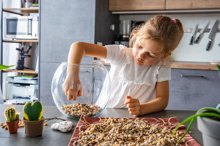Little girl pouring stones into glass container to create drainage for future florarium or closed ecosystem. Hands-on learning, eco-friendly creativity and early involvement in nature-based projects.の写真素材