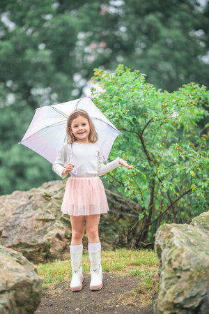 Little girl smiling and holding out her hands to catch raindrops while standing under an umbrella. Joyful exploration of weather and sensory experience in early childhood. High quality photoの写真素材