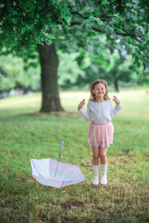Little girl jumping in the air next to a closed umbrella lying on the ground. A burst of energy and spontaneous happiness on a rainy day. High quality photoの写真素材