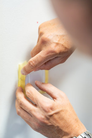 Man covering a light switch with masking tape before painting the wall white. Home renovation,...