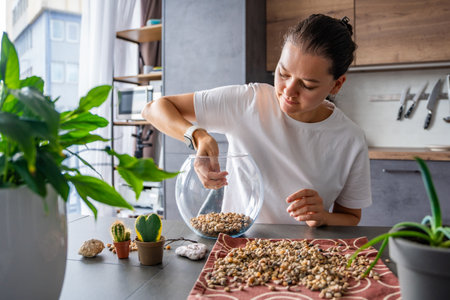Young woman pouring stones into a glass container while preparing a terrarium. Concept of mindful crafting, eco-friendly lifestyle and home plant design. High quality photoの写真素材