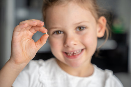 Portrait of a smiling girl holding her milk tooth between her fingers. Focus is on the tooth in her...