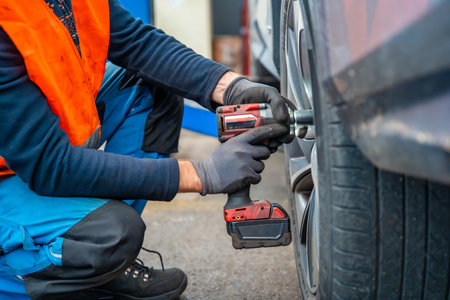 Mechanic using an impact wrench to remove lug nuts from a car wheel. Seasonal tire change and...