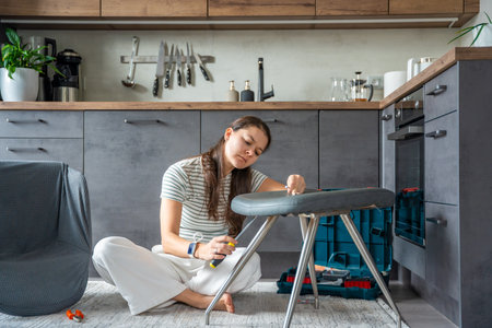 Frustrated young woman trying to assemble a chair with tools on the floor. Concept of difficulty and struggle in do it yourself project. High quality photoの写真素材