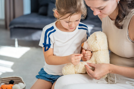 Mother and daughter sewing a plush teddy bear together during a home repair activity. Teaching children to care for belongings and embrace sustainable habits through hands-on experience..の写真素材