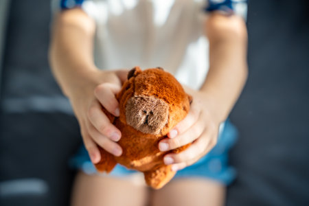 A plush capybara toy held in a child hands. The image reflects Gen Z love for internet-inspired mascots and the aesthetic comfort culture of soft toys. High quality photoの写真素材